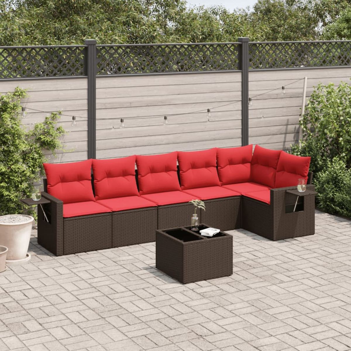 Outdoor-Ecksofa mit roten Kissen und einem Couchtisch auf einer gepflasterten Terrasse. Ein Zaun und Grün im Hintergrund.
