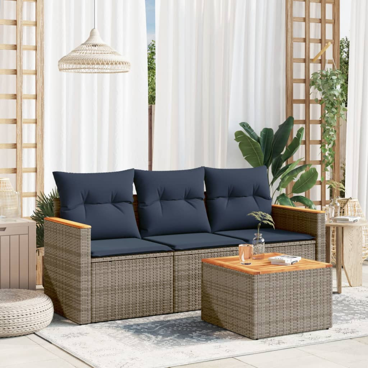 Outdoor-Sitzarrangement. Korbanlage mit blauen Kissen und einem Couchtisch. Weiße Vorhänge, Pflanzen und eine Pendelleuchte.