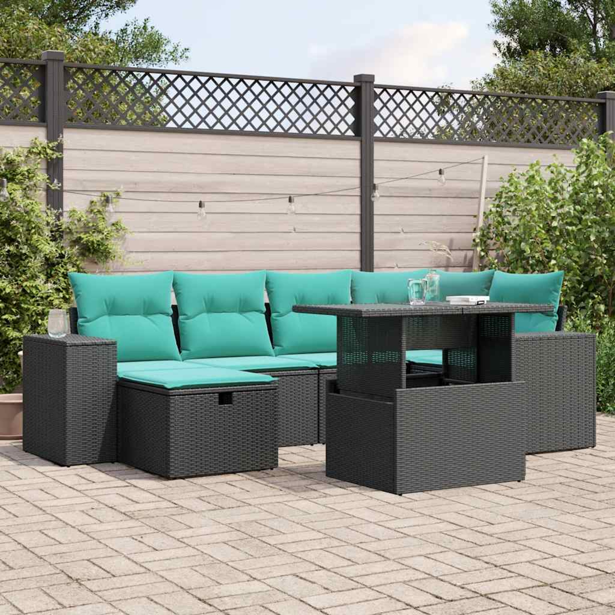 Terrassenmöbel-Set mit grauen Korbmöbeln, türkisfarbenen Kissen und einem Tisch mit Hubfunktion. Im Hintergrund ein Holzzaun und Grün.