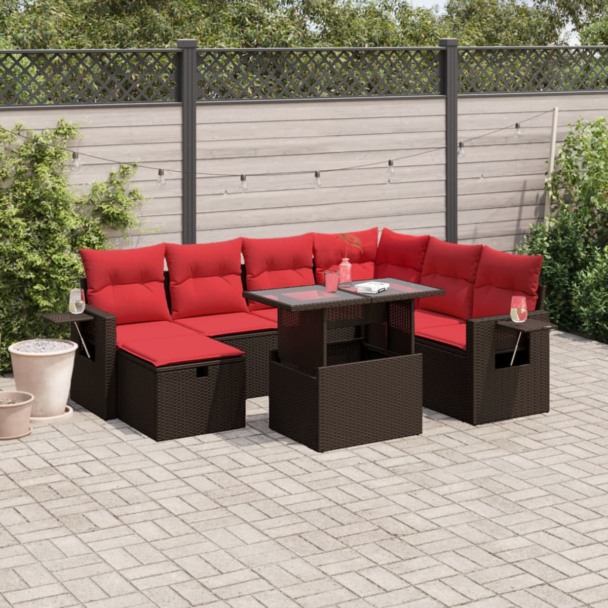 Outdoor-Ecksofa mit roten Kissen und einem Tisch mit Glasplatte auf einer Backstein-Terrasse. Im Hintergrund ein Zaun und Grün.