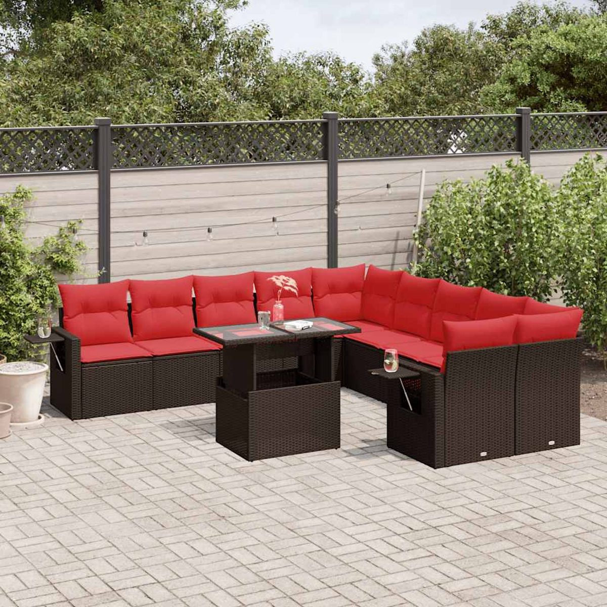 Ein Outdoor-Ecksofa mit roten Kissen und einem Couchtisch mit Glasplatte auf einer Steinterrasse. Der Hintergrund umfasst einen Zaun und Grün.