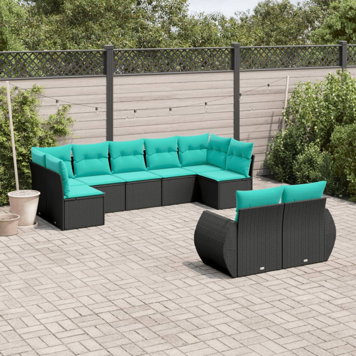 Szene im Freien mit dunkelgrauem Korbschnittsofa und türkisfarbenen Kissen auf einer Ziegelterrasse. Grüne Pflanzen und ein Zaun im Hintergrund.