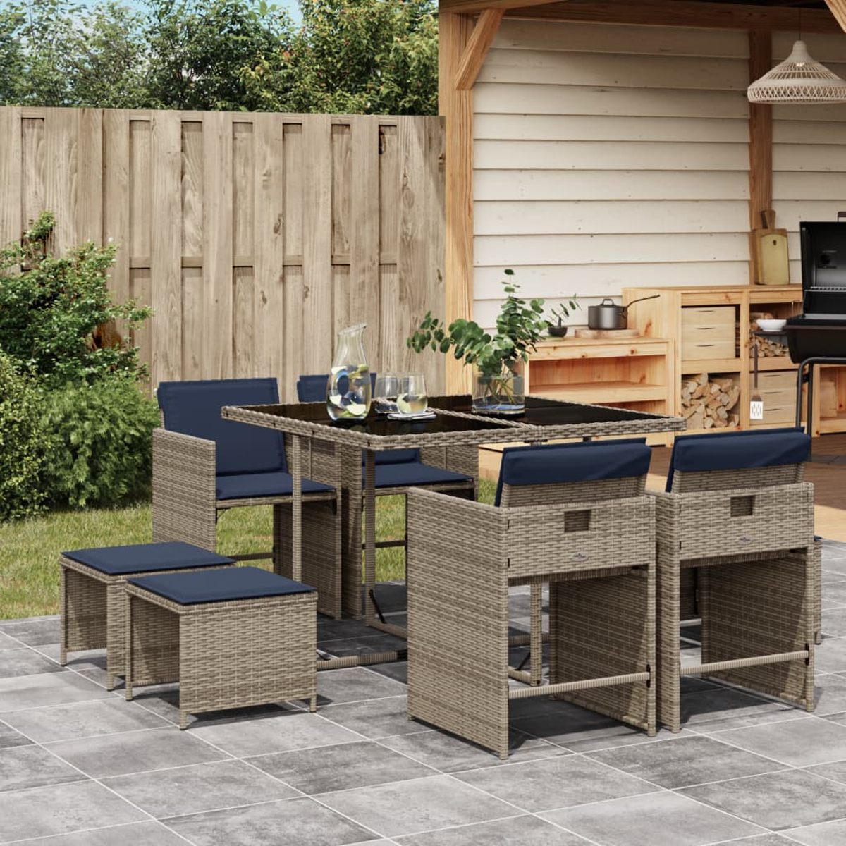 Essgruppe im Freien mit Tisch, Stühlen und Hockern auf einer Terrasse. Im Hintergrund ein Holzzaun und ein Schuppen.