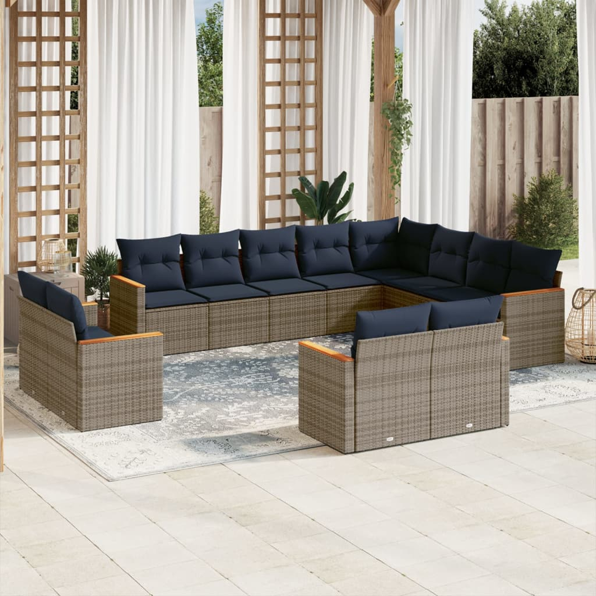 Outdoor-Ecksofa mit marineblauen Kissen. Korbmöbel auf einem Teppich. Gardinen und Spalier im Hintergrund. Sonnige Umgebung im Freien.