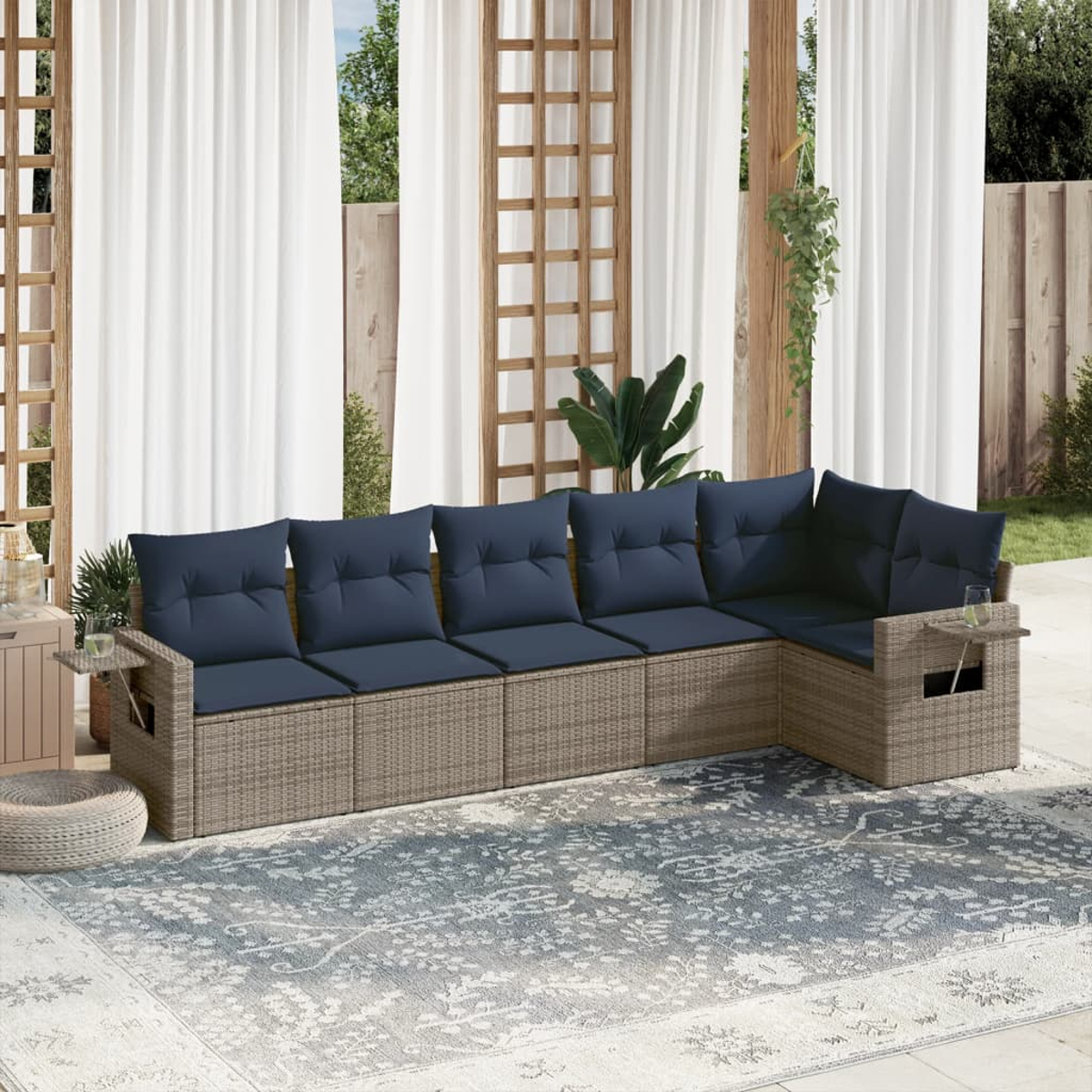 Ein Ecksofa im Freien mit blauen Kissen steht auf einem gemusterten Teppich. Vorhänge und Pflanzen sind im Hintergrund, mit einer Holzstruktur.