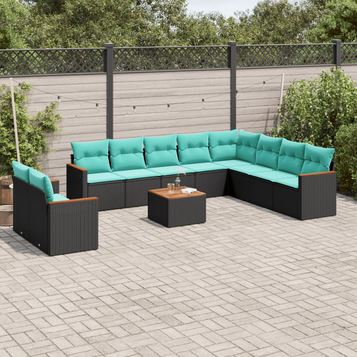 Garten-Sitzgruppe mit türkisfarbenen Kissen, schwarzen Korbflechtrahmen und einem kleinen Holztisch auf einer Ziegelterrasse.