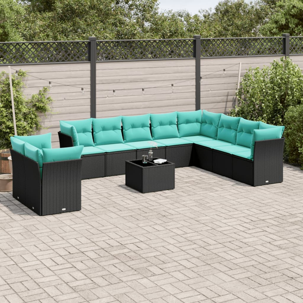 Sofá seccional al aire libre con cojines turquesa y una mesa de centro negra en un patio de ladrillos. Follaje verde y una valla al fondo.