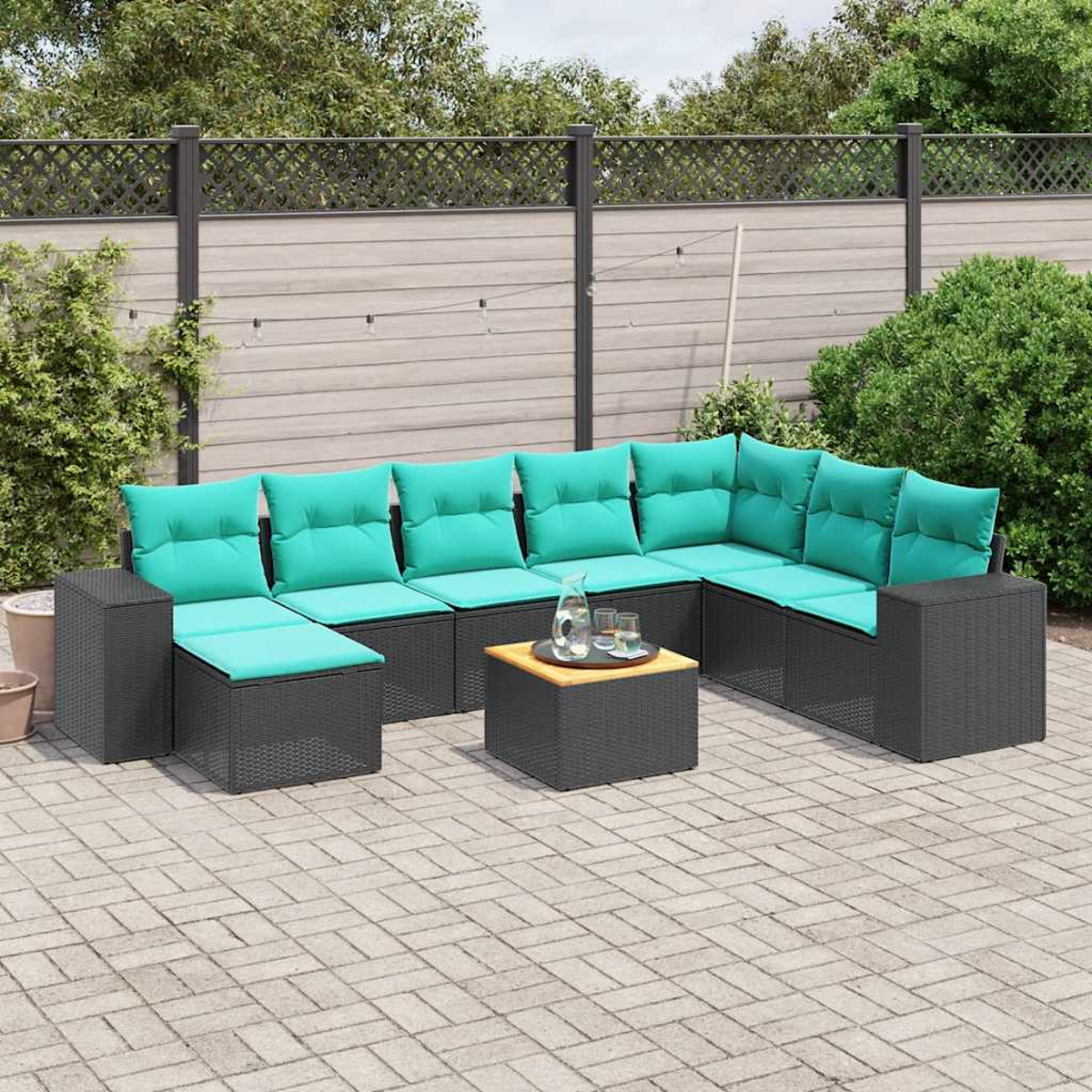 Ein Outdoor-Terrassen-Set mit türkisfarbenen Kissen. Ein kleiner Tisch hat eine Glaskaraffe und Gläser. Schwarze Korbmöbel stehen auf einer Steinterrasse.