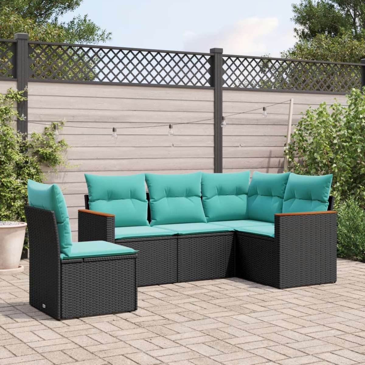 Outdoor-Ecksofa mit türkisfarbenen Kissen und schwarzem Korbgewebe, mit passendem Stuhl, auf einer Terrasse. Im Hintergrund sind ein Zaun und Pflanzen zu sehen.