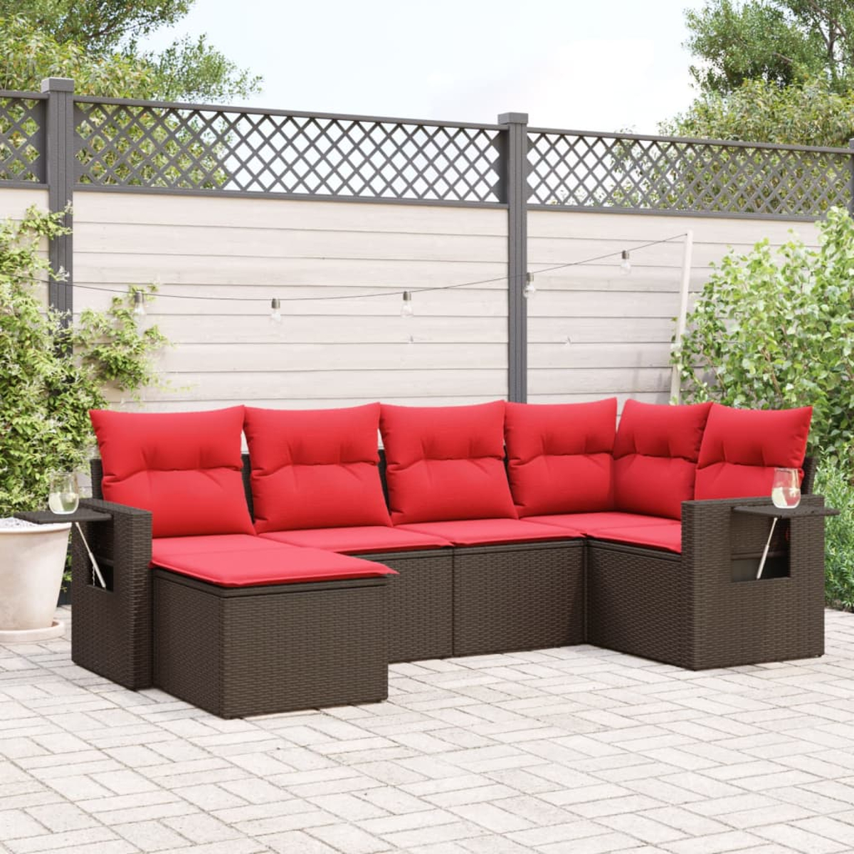 Ein Ecksofa mit roten Kissen steht auf einer Terrasse. Ein Gitterzaun und Grünzeug befinden sich im Hintergrund.