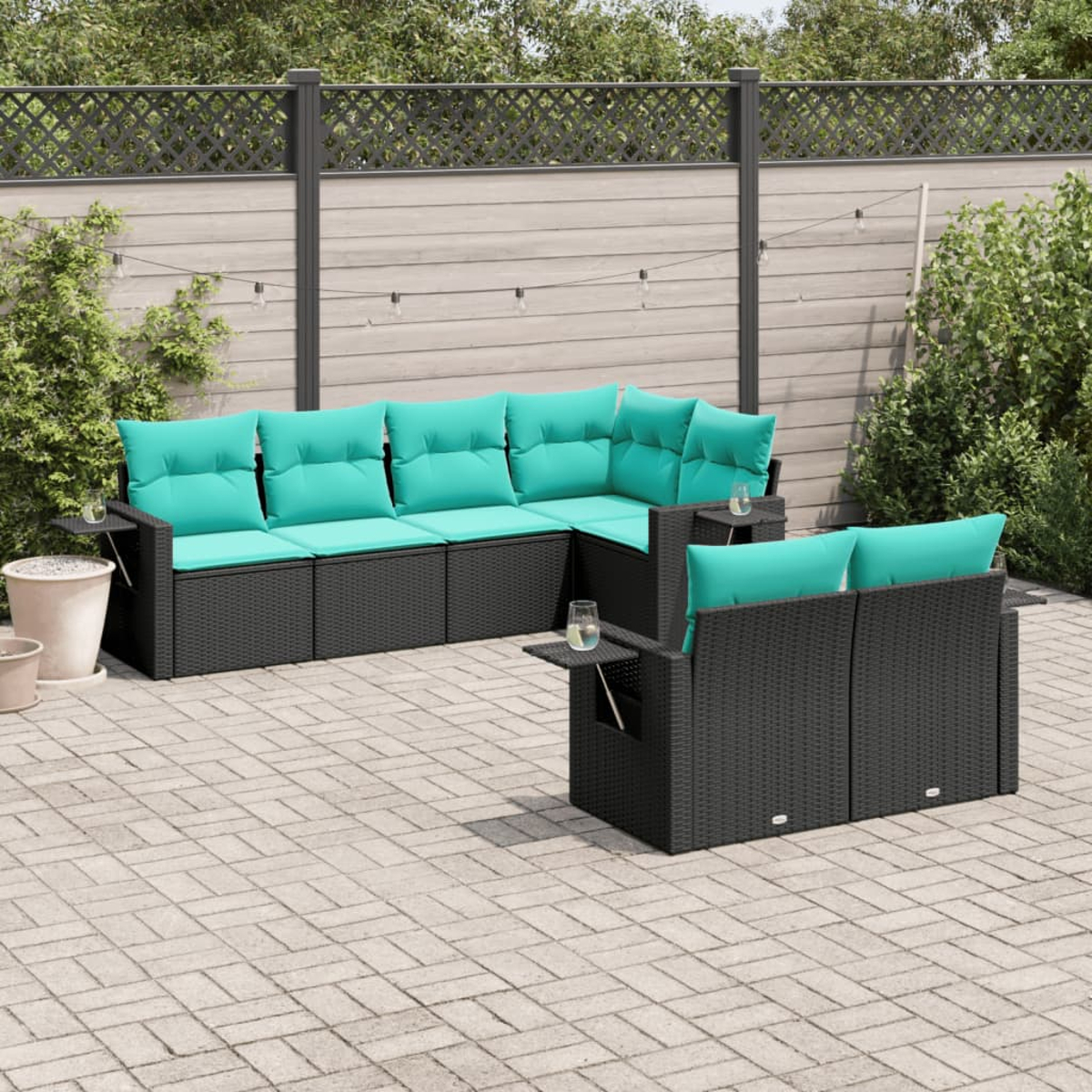 Terrassenset mit schwarzen Korbmöbeln und türkisfarbenen Kissen. Eine Terrasse mit Zaun im Hintergrund.