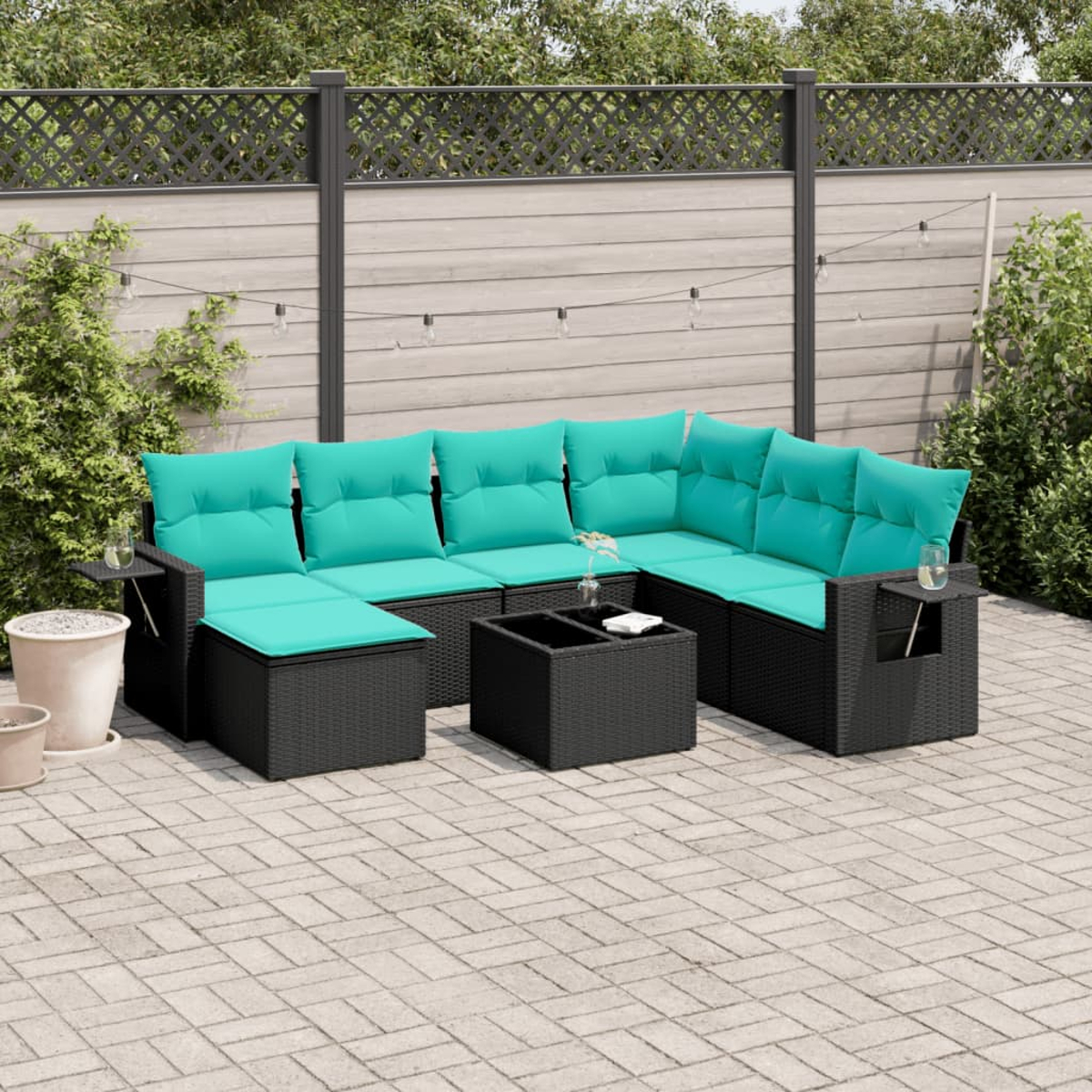 Outdoor-Ecksofa mit türkisfarbenen Kissen, schwarzem Korbgewebe auf einer Terrasse. Enthält einen Couchtisch. Im Hintergrund befinden sich ein Zaun und Grün.