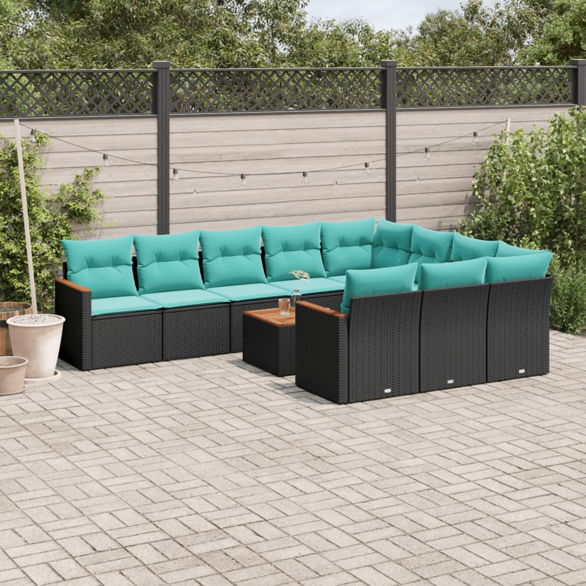 Garten-Sitzgruppe mit türkisfarbenen Kissen auf schwarzen Korbgeweben. Davor steht ein kleiner Holztisch. Im Hintergrund befinden sich ein Zaun und Bäume.