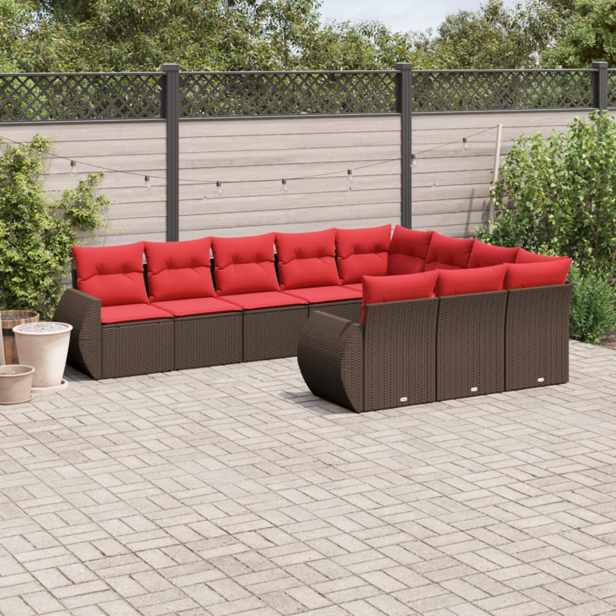 Outdoor-Ecksofa mit roten Kissen auf einer Ziegelterrasse. Hintergrund: Zaun, Grün und Lichterketten.