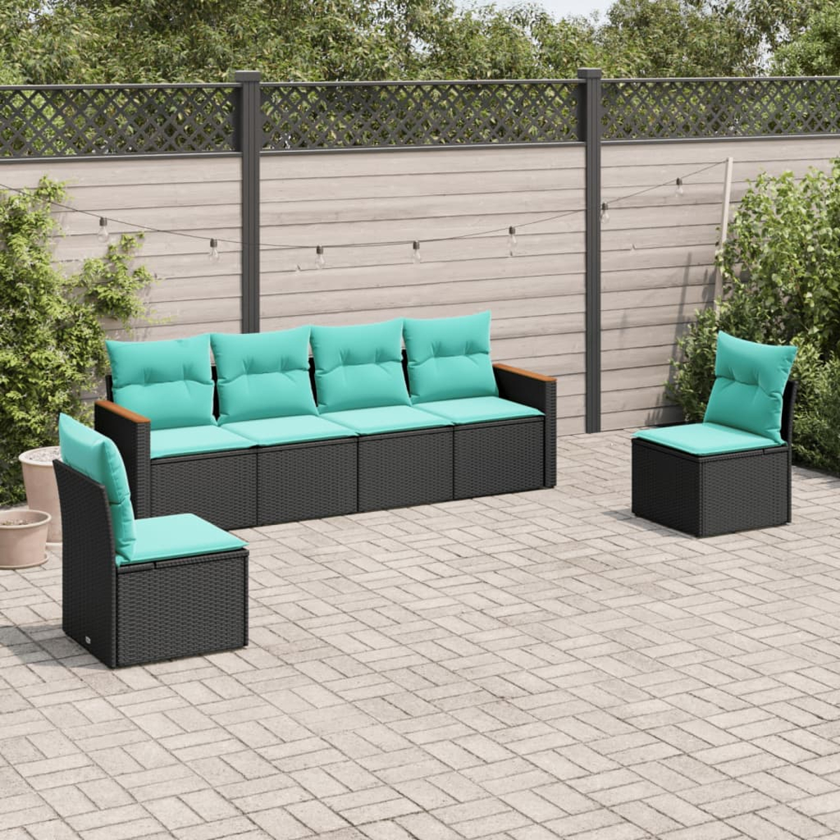 Terrassenset: schwarzes Korbmöbel-Sofa und Stühle mit türkisfarbenen Kissen. Auf einer gepflasterten Terrasse, mit Zaun und Grün im Hintergrund.