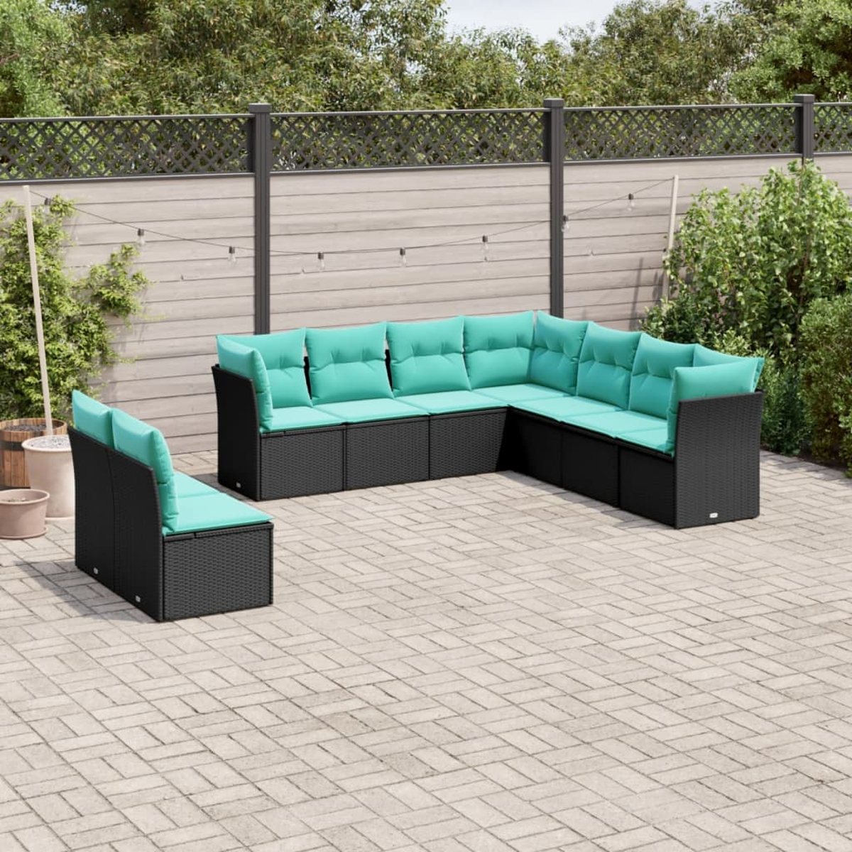 Ein Ecksofa im Freien mit türkisfarbenen Kissen steht auf einer Terrasse. Das Sofa ist schwarz, der Hintergrund umfasst einen Zaun und Grün.
