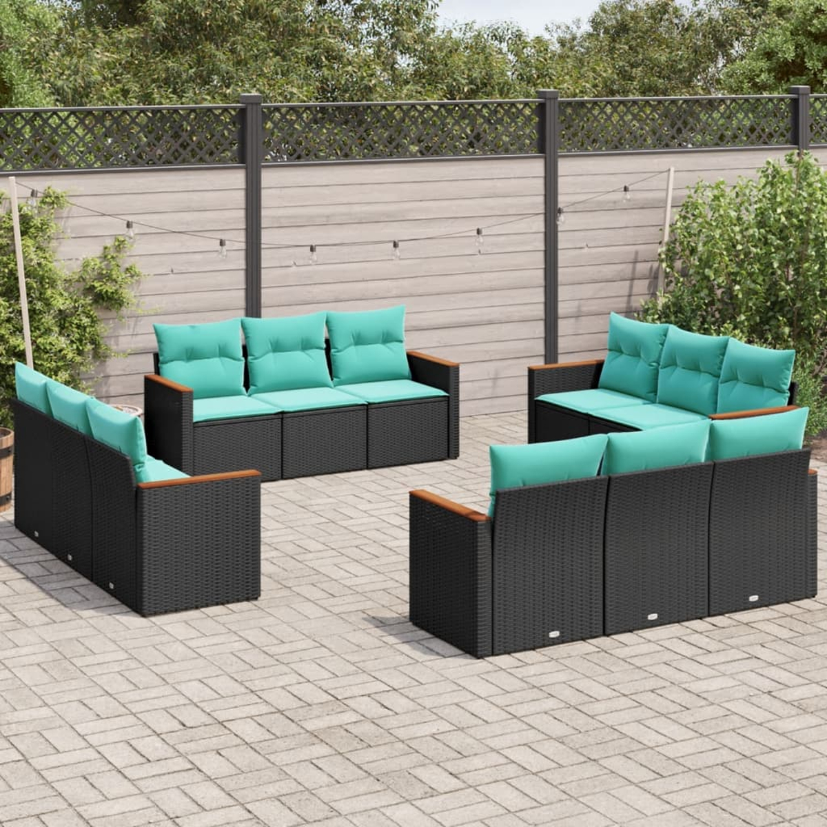 Gartenmöbel-Set mit schwarzen Korbflechtrahmen und türkisfarbenen Kissen auf einer gepflasterten Terrasse, vor einem Holzzaun und Grün.