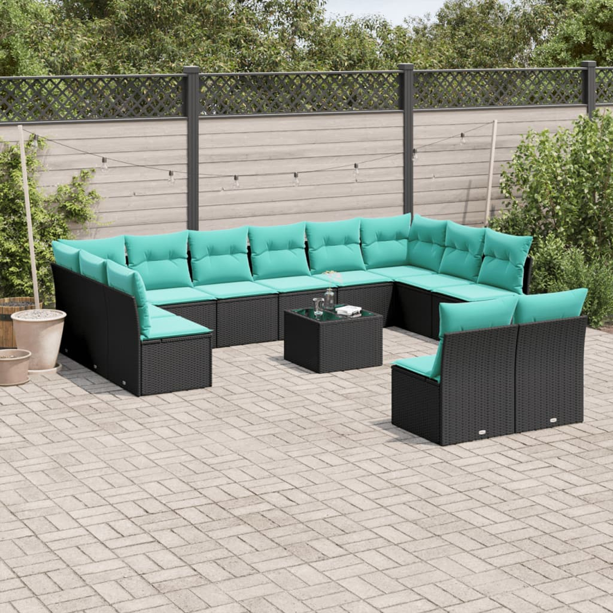 Outdoor-Ecksofa mit türkisfarbenen Kissen und schwarzem Korbgeflecht. Enthält einen kleinen Tisch. Auf einer Steinterrasse mit Zaun im Hintergrund.