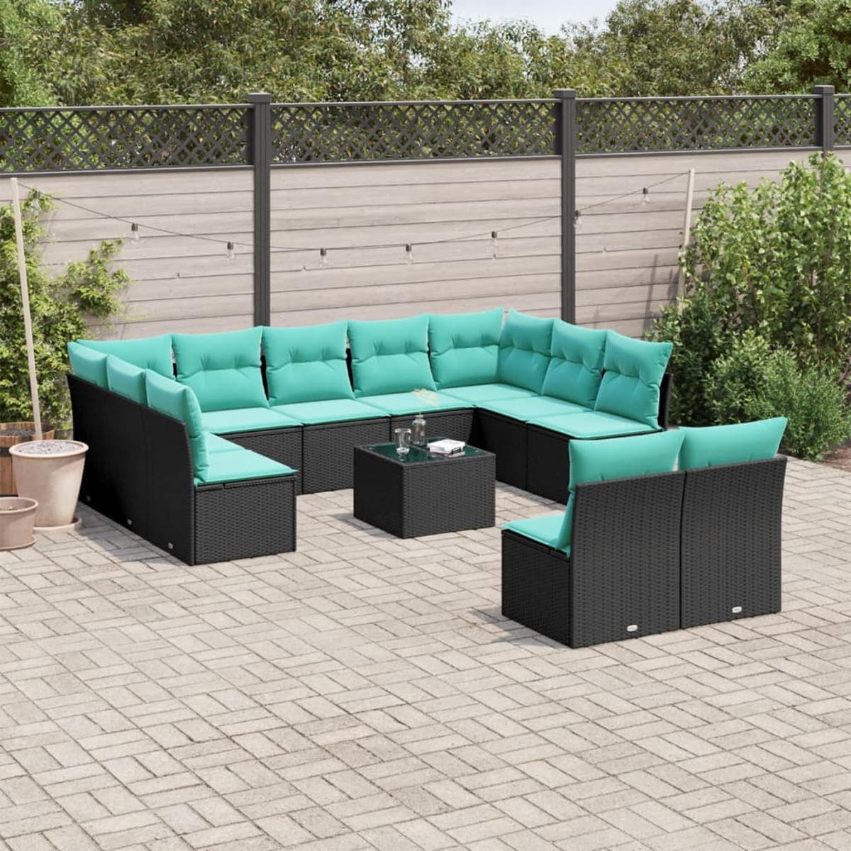 Outdoor-Ecksofa mit tealfarbenen Kissen auf einer gepflasterten Terrasse. Ein schwarzer quadratischer Tisch steht in der Mitte.