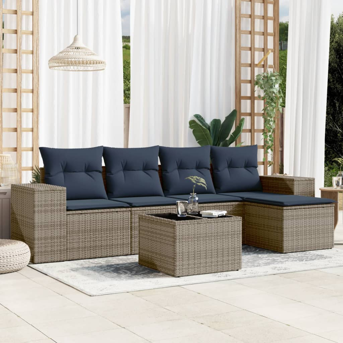 Outdoor-Wicker-Sofa mit marineblauen Kissen und einem passenden Couchtisch. Weiße Vorhänge im Hintergrund. Eine gewebte Pendelleuchte hängt darüber.