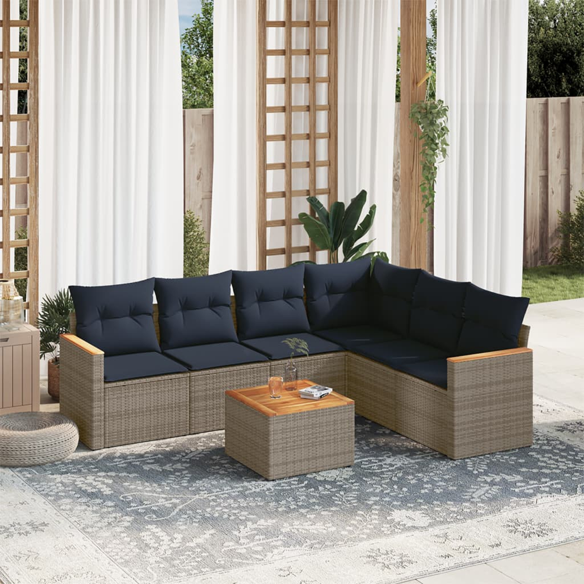 Sofá seccional exterior con cojines azul marino sobre una alfombra estampada. Incluye mesa de café de madera y cortinas blancas.