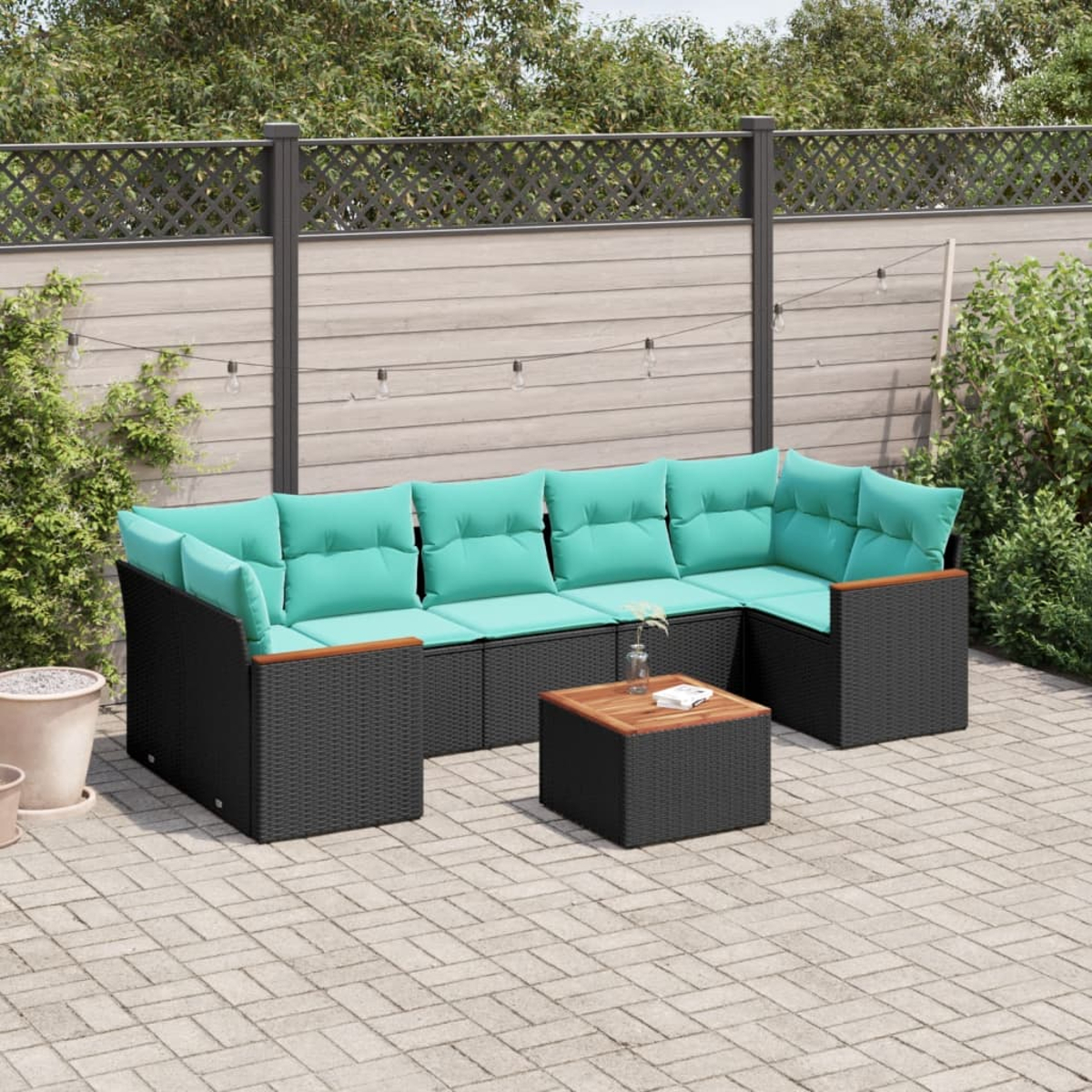 Outdoor-Ecksofa mit türkisfarbenen Kissen und einem Holztisch auf einer gepflasterten Terrasse, im Hintergrund ein Holzzaun.