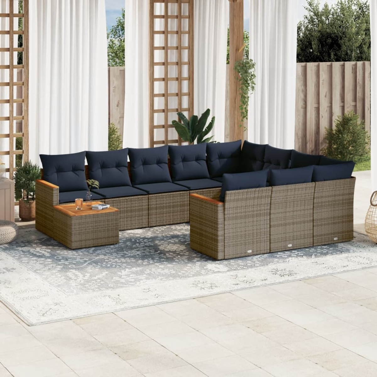 Sofá seccional exterior con cojines azul marino sobre una alfombra estampada. Cortinas blancas y estructuras de madera al fondo.