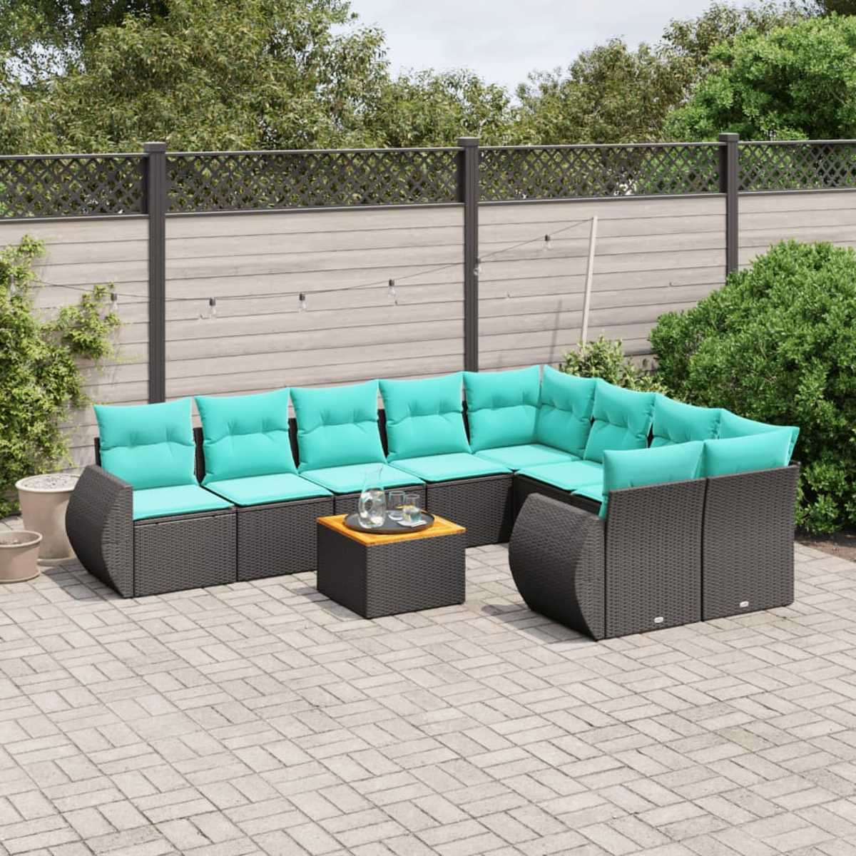 Outdoor-Ecksofa mit türkisfarbenen Kissen und einem kleinen Tisch. Die Szene spielt auf einer Terrasse mit Zaun und Grün im Hintergrund.