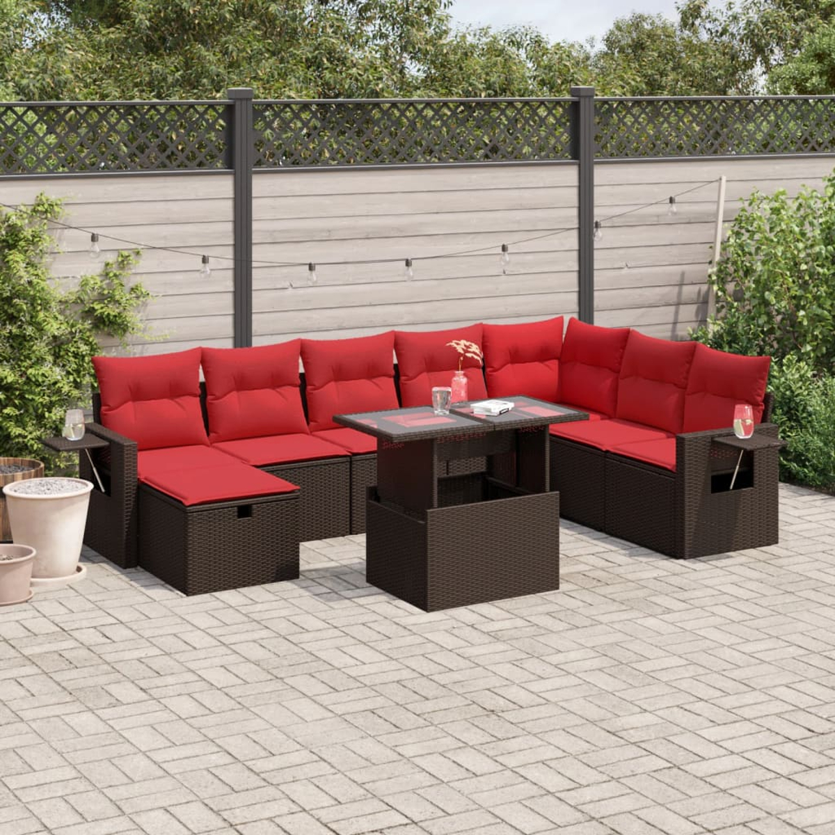 Garten-Sitzgruppe mit roten Kissen auf braunen Korbmöbeln. Ein Tisch mit Glasplatte steht in der Mitte. Der Hintergrund umfasst einen Zaun und Pflanzen.