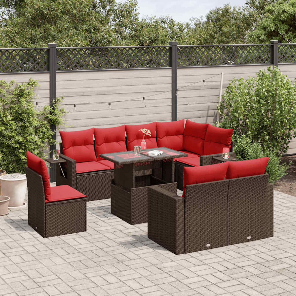 Terrassenmöbel-Set mit braunen Korbmöbeln und roten Kissen. Tisch und Stühle sind auf einer Ziegelterrasse angeordnet.