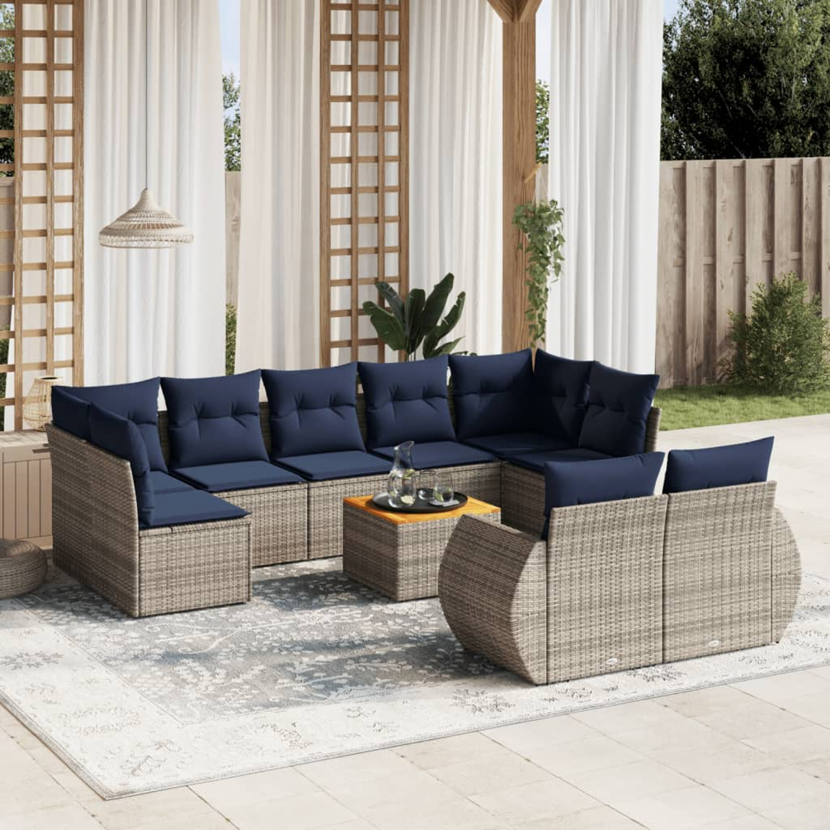 Outdoor-Sitzbereich mit Ecksofa, blauen Kissen, einem Teppich und einem kleinen Tisch. Weiße Vorhänge und Holzstrukturen im Hintergrund.