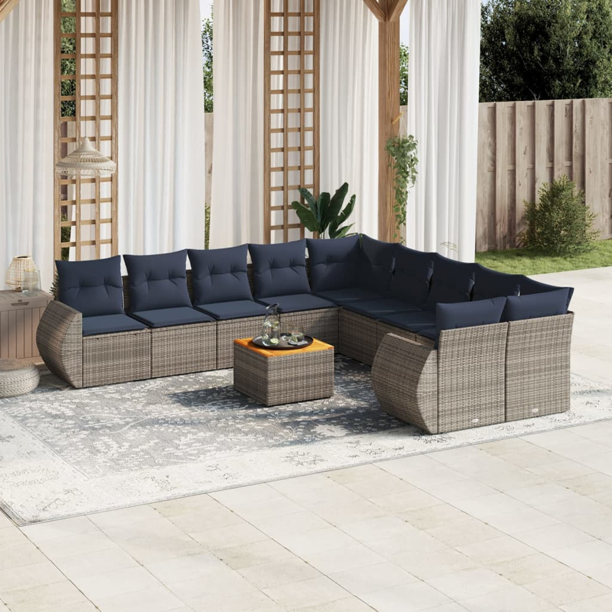 Ein Ecksofa im Freien mit marineblauen Kissen, einem kleinen Tisch und einem Teppich auf einer Terrasse. Der Hintergrund umfasst Vorhänge, Bäume und einen Zaun.