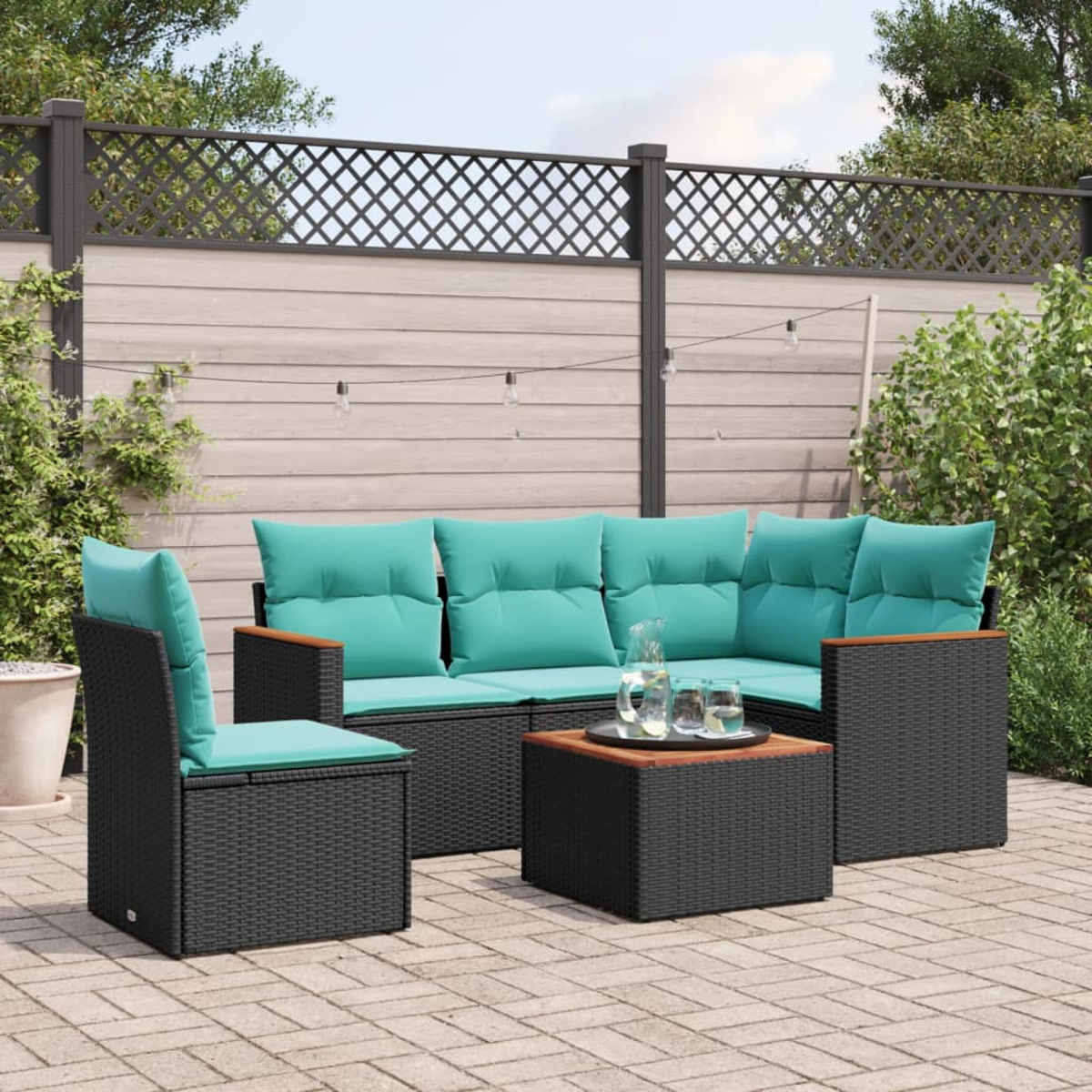 Garten-Terrassenset: schwarzes Korbmöbel mit türkisfarbenen Kissen, Couchtisch, Stuhl. Hinterhof mit Zaun und Pflanzen. Sonniger Tag.