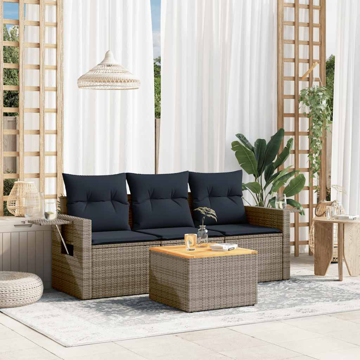 Asientos al aire libre con un sofá tejido, cojines azul oscuro y una mesa de centro de madera. Cortinas blancas forman el fondo.