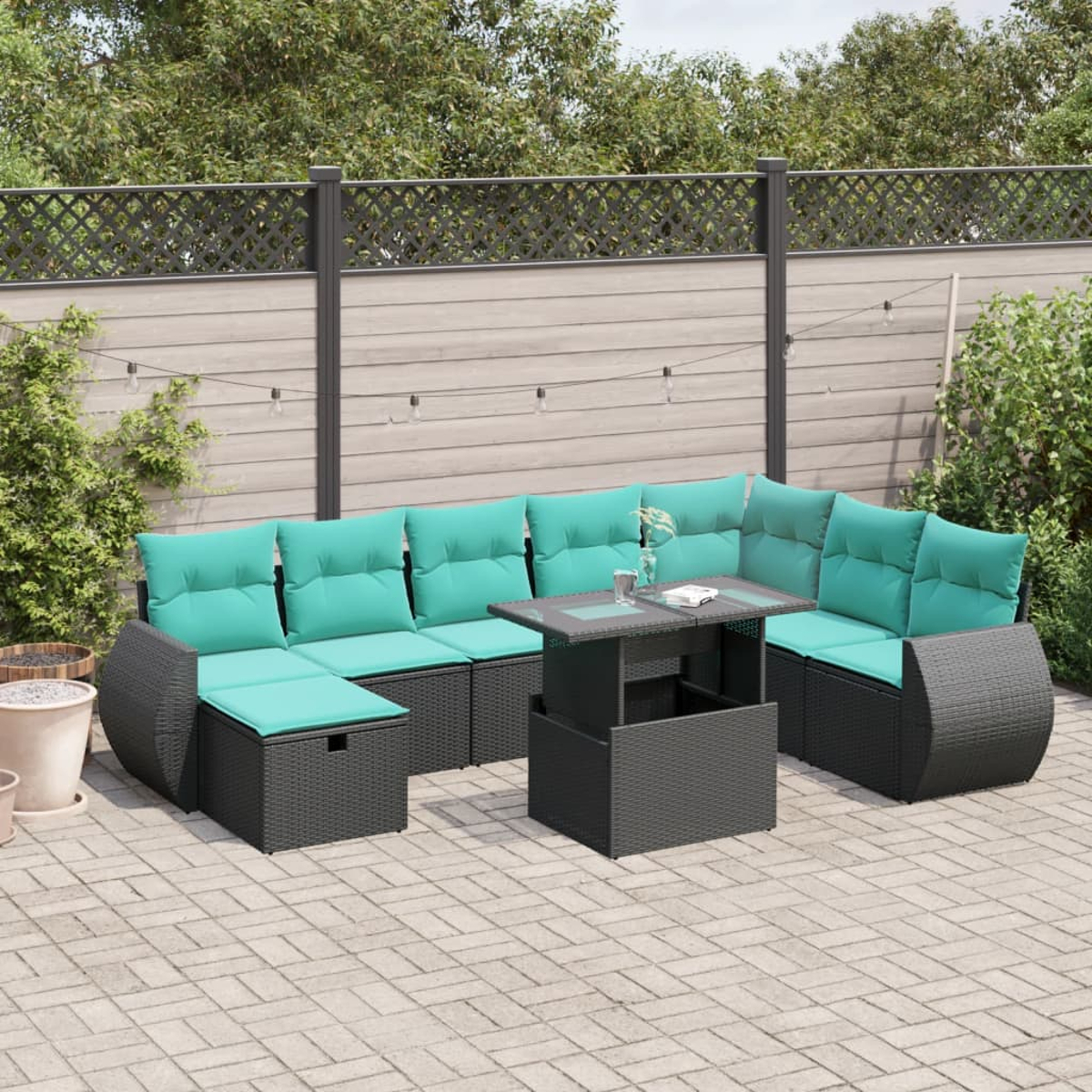 Gartenmöbel-Set. Schwarzes Korbsessel-Sofa mit türkisfarbenen Kissen. Mit einem Tisch mit Hebefunktion. Auf einer Ziegelterrasse in der Nähe eines Zauns.