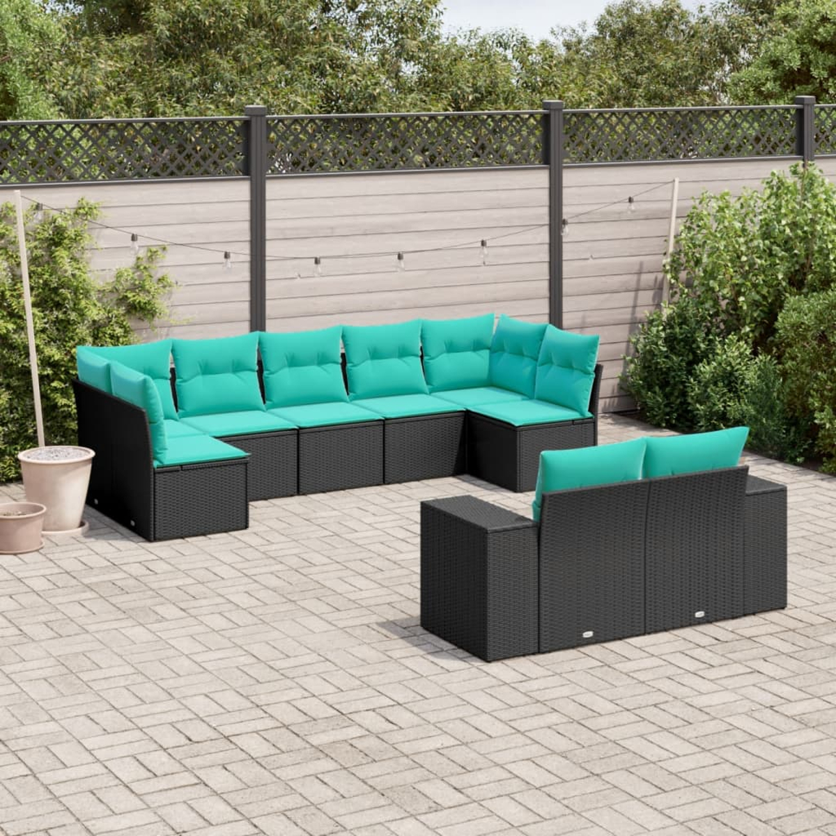 Juego de patio al aire libre con muebles de mimbre negro y cojines turquesa. Situado en un patio pavimentado, con una valla y vegetación de fondo.