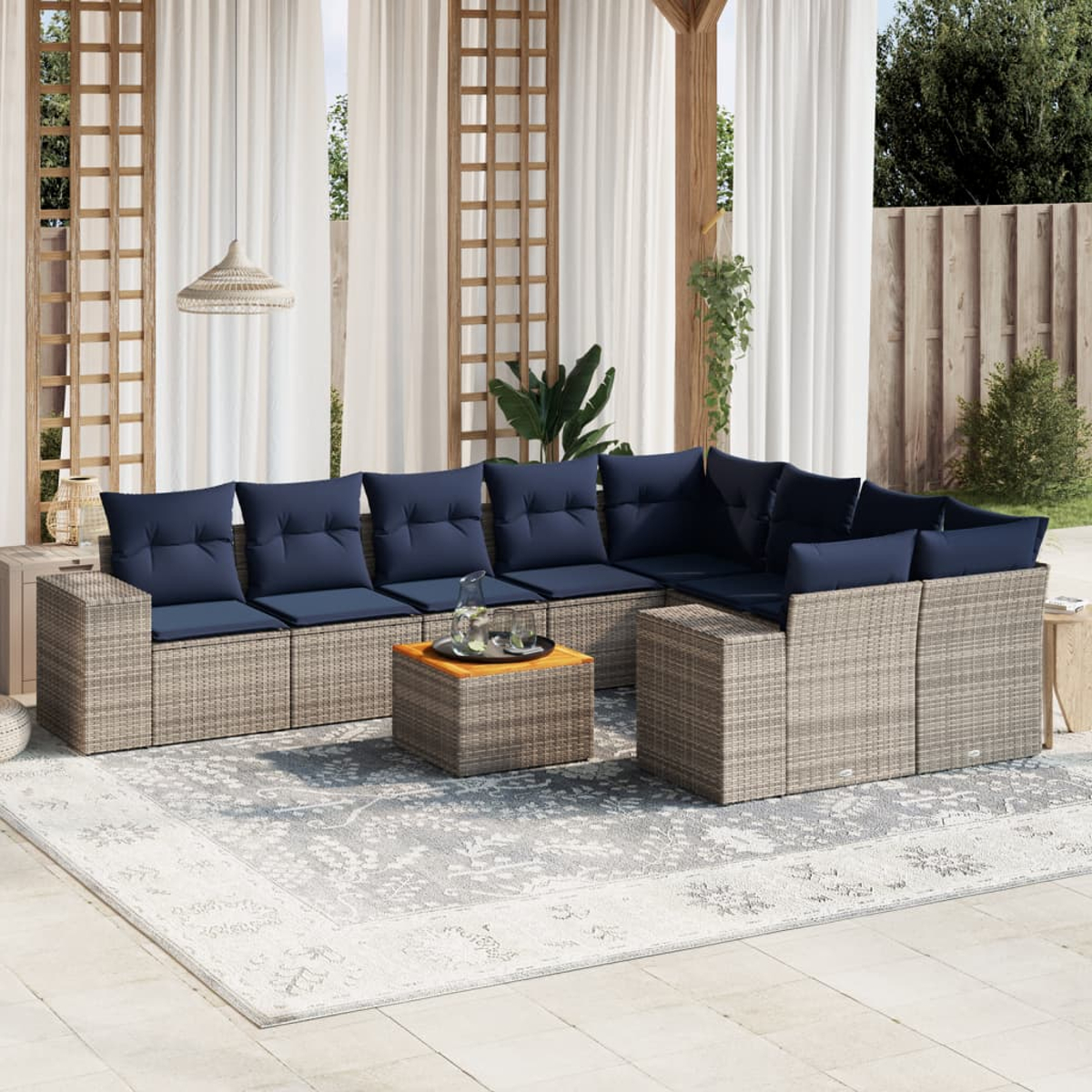 Outdoor-Ecksofa mit marineblauen Kissen und einem Couchtisch auf einem gemusterten Teppich. Der Hintergrund umfasst transparente Vorhänge und Holzelemente.