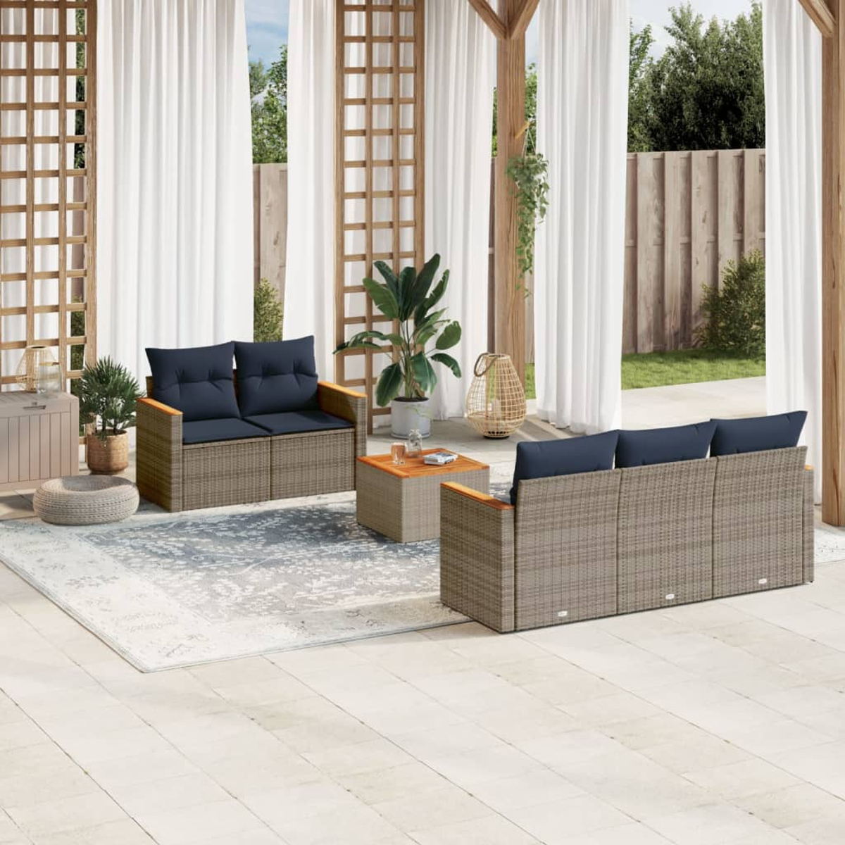 Terrassenset mit grauen Korbsesseln, marineblauen Kissen, Holztisch, Teppich, weißen Vorhängen und Pflanzen.