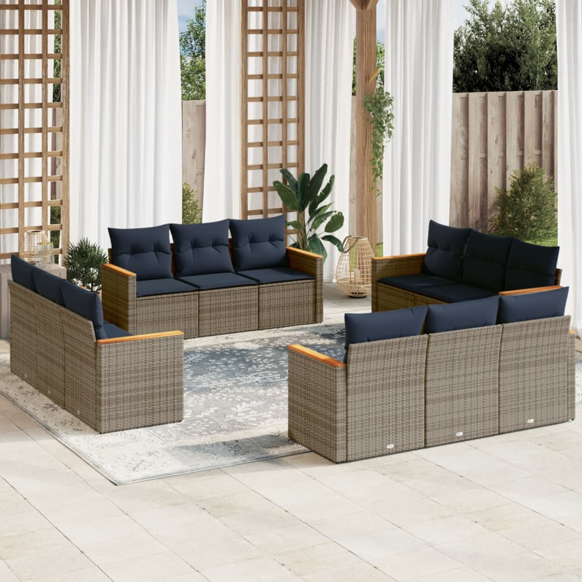 Juego de muebles de exterior. Sofás y sillas de mimbre con cojines azules dispuestos en un patio con cortinas y plantas al fondo.