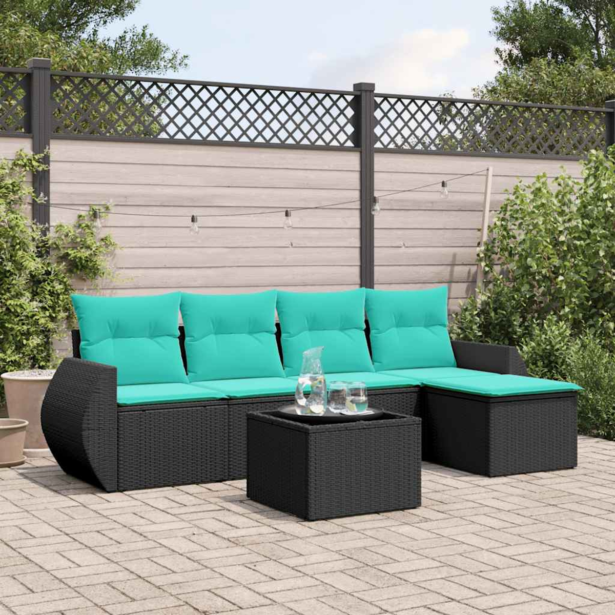 Garten-Terrassenset mit schwarzen Korbmöbeln und türkisfarbenen Kissen. In der Mitte steht ein kleiner Tisch mit Wasserkrug.