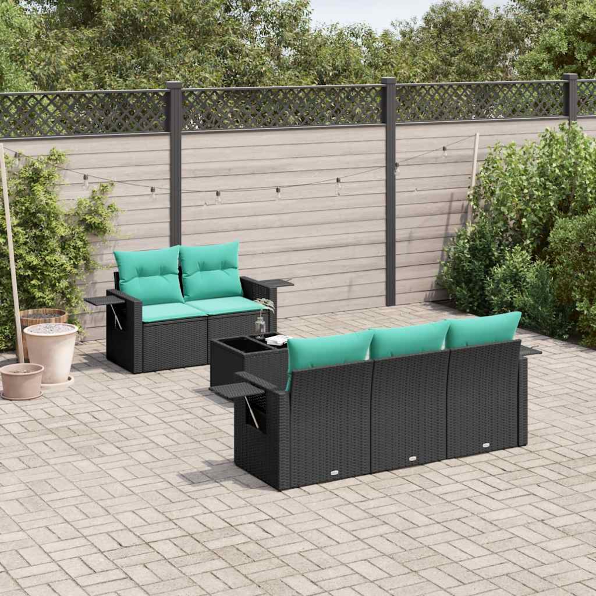Garten-Sitzgruppe mit schwarzem Korbmöbeln und tealfarbenen Kissen auf einer gepflasterten Terrasse. Ein Holzzaun mit Laub im Hintergrund.