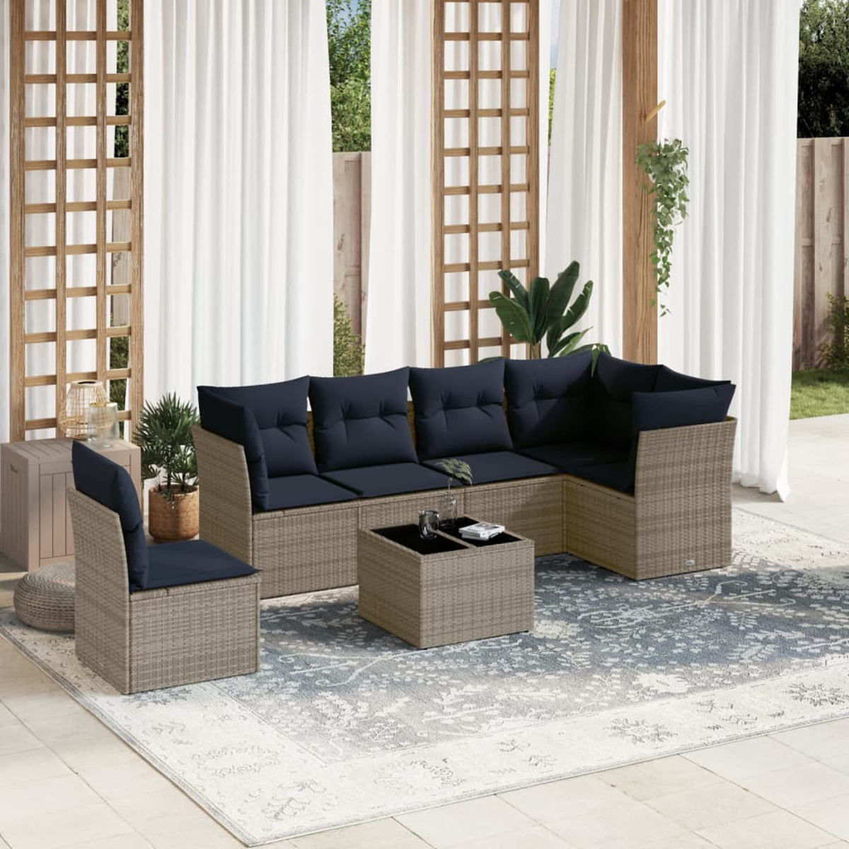 Juego de patio al aire libre con sofá seccional, silla y mesa de centro. Cojines azul marino, marcos de ratán. Cortinas blancas y alfombra estampada.