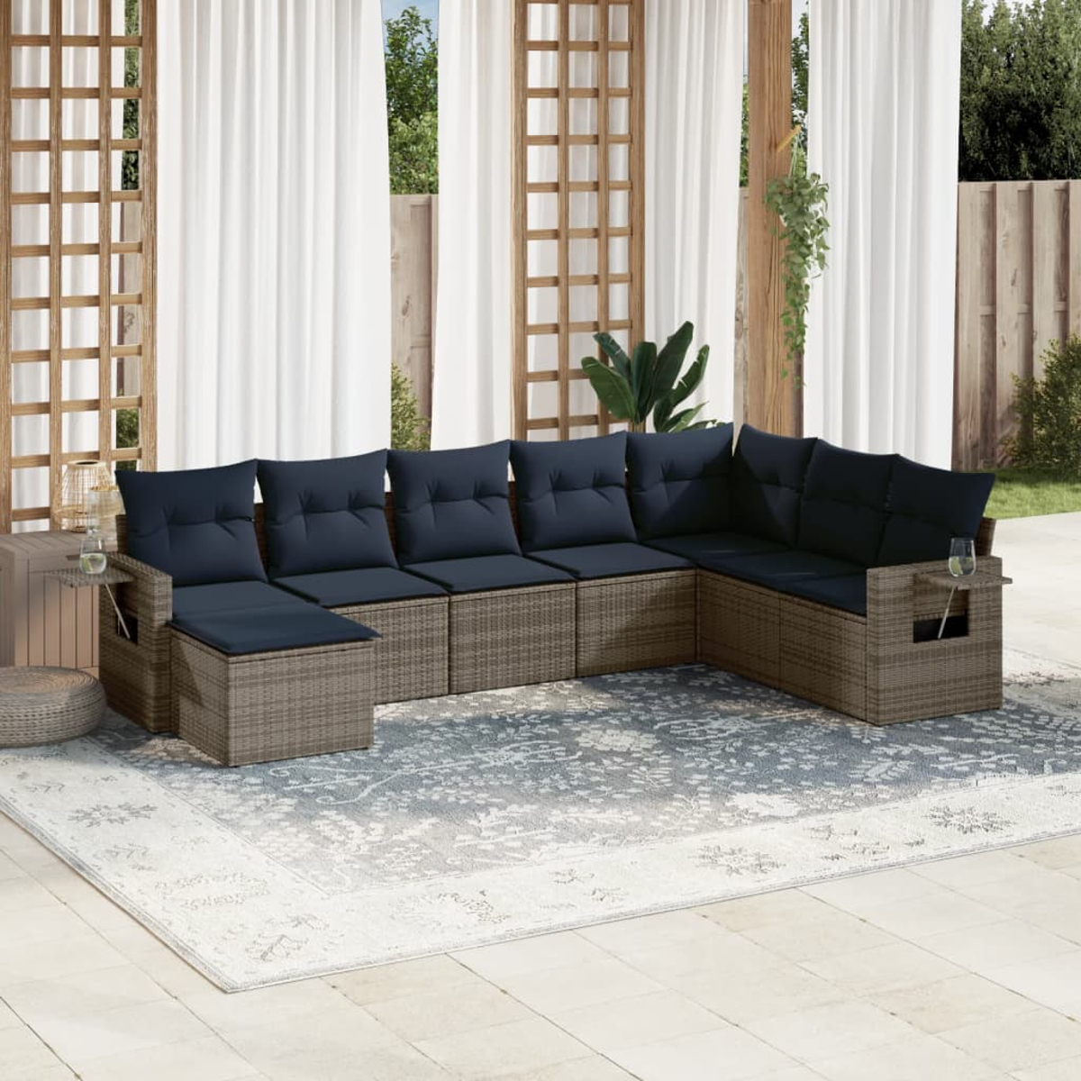 Ein Ecksofa im Freien mit marineblauen Kissen steht auf einem gemusterten Teppich. Weiße Vorhänge und Holzrahmen befinden sich hinter dem Sofa.