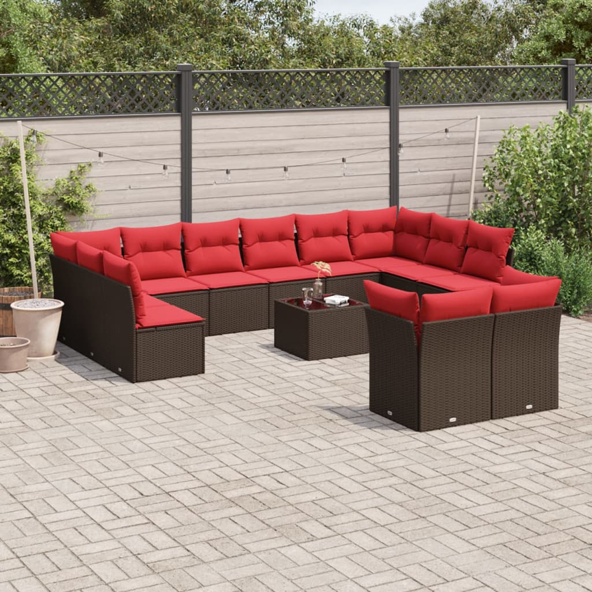 Garten-Sitzgruppe mit roten Kissen. Ein Couchtisch und ein paar Pflanzen sind ebenfalls zu sehen. Der Hintergrund zeigt einen Zaun und einige Bäume.