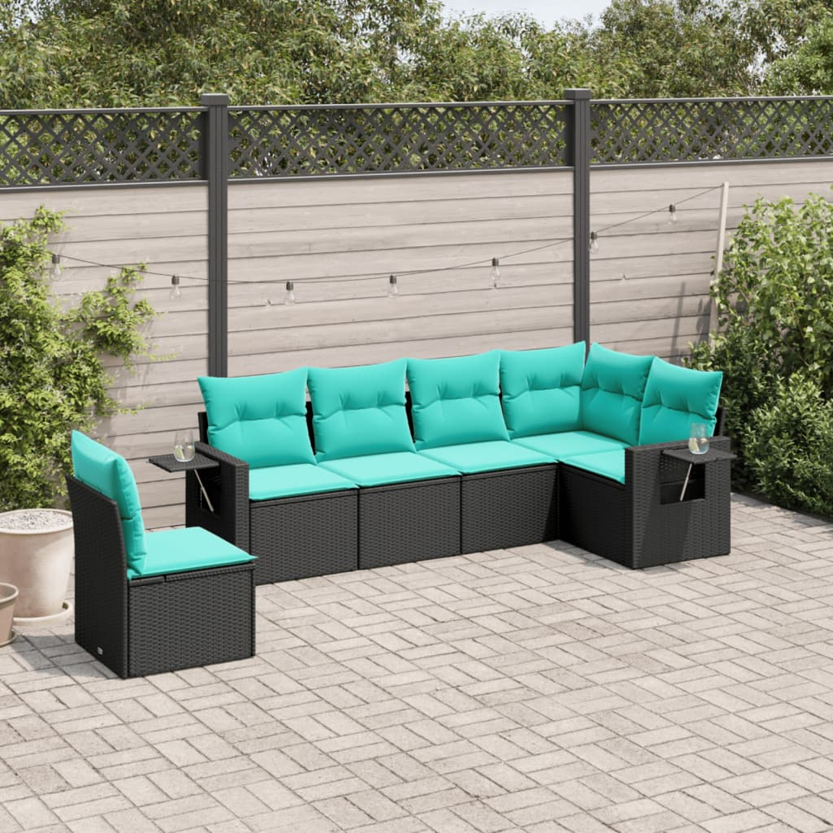 Garten-Set: schwarzes Korbmöbel-Sofa mit türkisfarbenen Kissen, passendem Stuhl und Beistelltischen auf einer gepflasterten Terrasse.