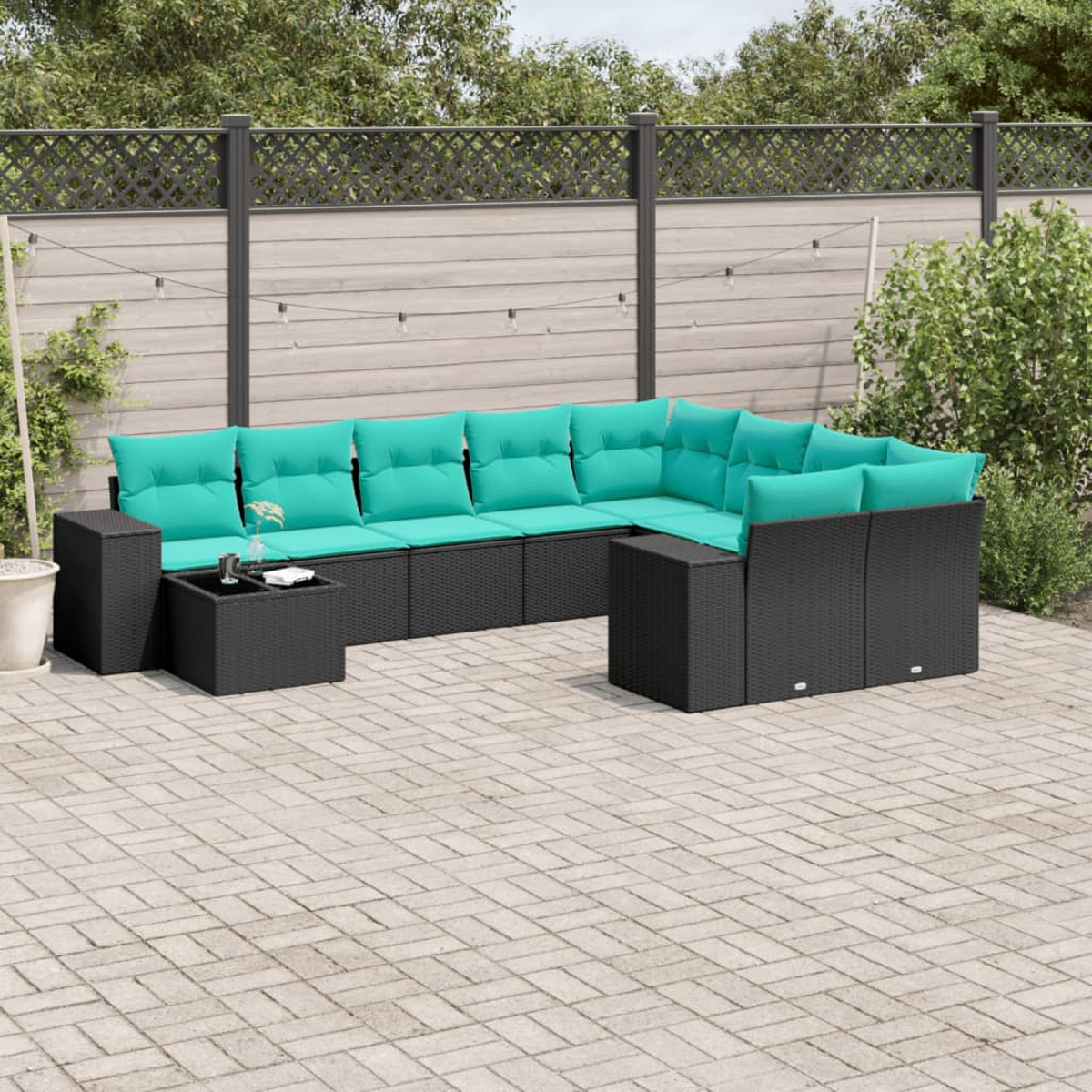 Terrassenset im Freien. Schwarze gewebte Möbel mit türkisfarbenen Kissen auf einer grauen Ziegelterrasse. Zaun und Laub im Hintergrund.
