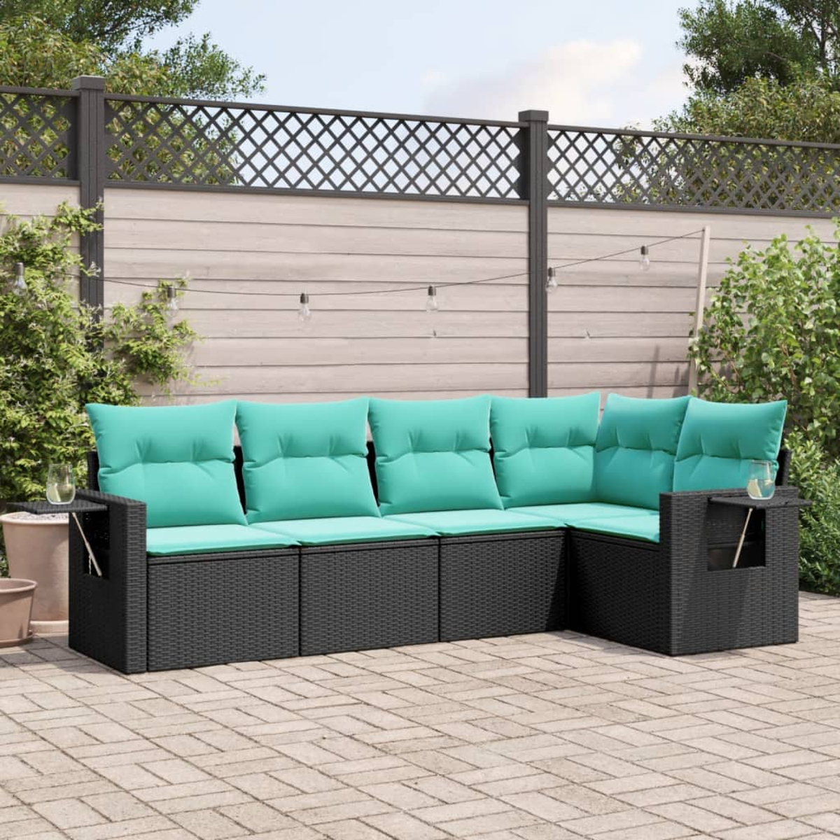 Ein Ecksofa im Freien mit türkisfarbenen Kissen steht auf einer Ziegelterrasse. Ein Holzzaun und Grünzeug sind im Hintergrund.