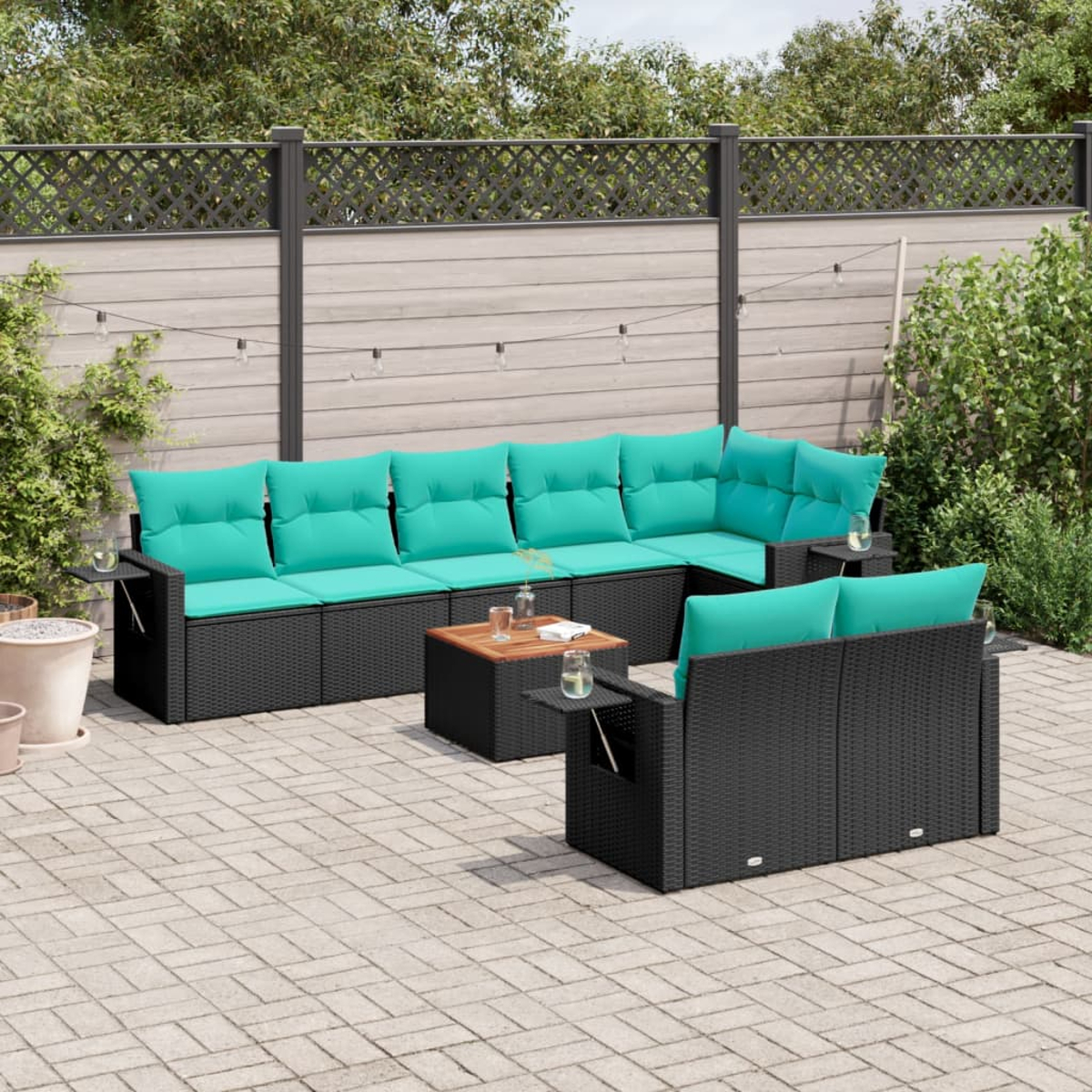Gartenmöbel-Set mit türkisfarbenen Kissen und schwarzen Korbflechtrahmen. Enthält einen Couchtisch. Hintergrund: Zaun, Pflanzen und Ziegelpflaster.