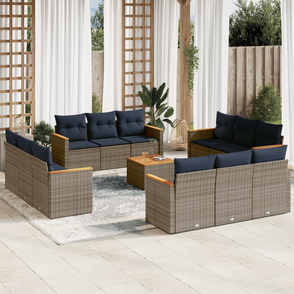 Outdoor-Sitzgruppe mit Korbmöbeln und blauen Kissen um einen Couchtisch. Weiße Vorhänge und Pflanzen im Hintergrund.
