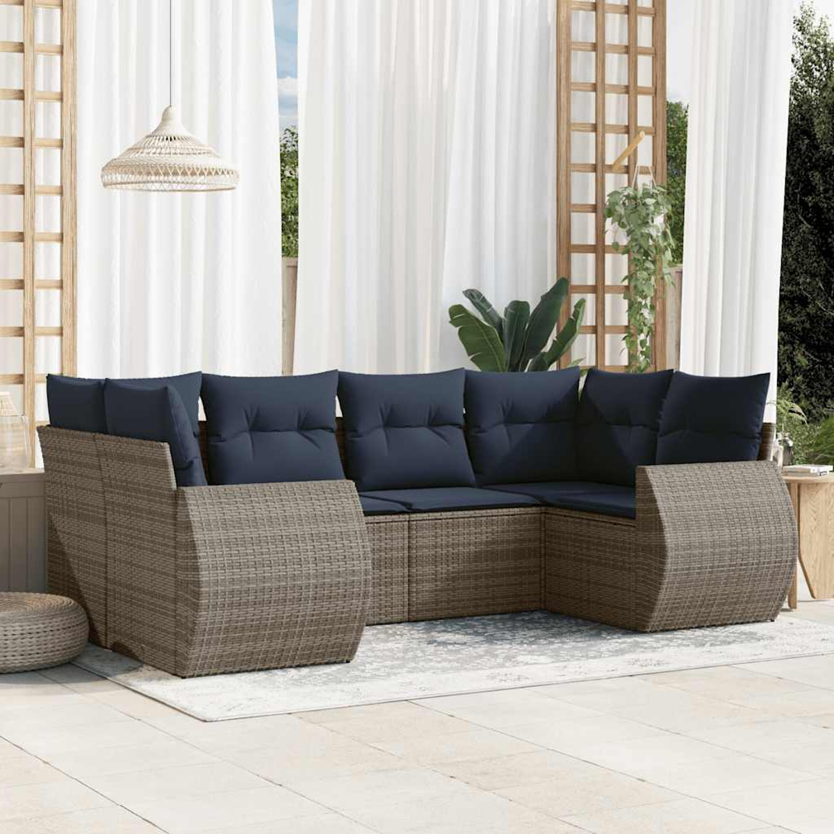 Ein Ecksofa für den Außenbereich mit marineblauen Kissen steht auf einer Terrasse. Über dem Sofa hängt eine gewebte Pendelleuchte. Weiße Vorhänge und ein Gitter im Hintergrund.